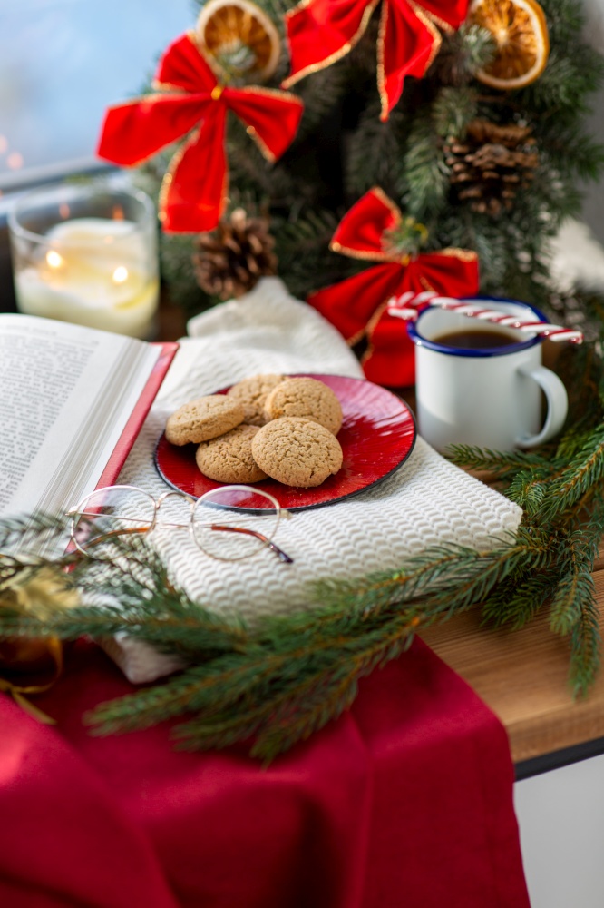 winter holidays and leisure concept - oatmeal cookies on red ceramic plate, cup of coffee, glasses and christmas decorations on window sill at home. oatmeal cookies on plate and christmas decor