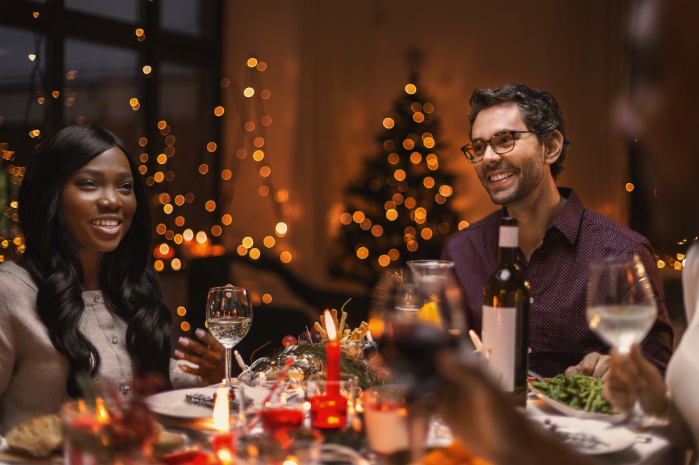 holidays and celebration concept - happy friends having christmas dinner at home and drinking red wine. happy friends drinking red wine at christmas party