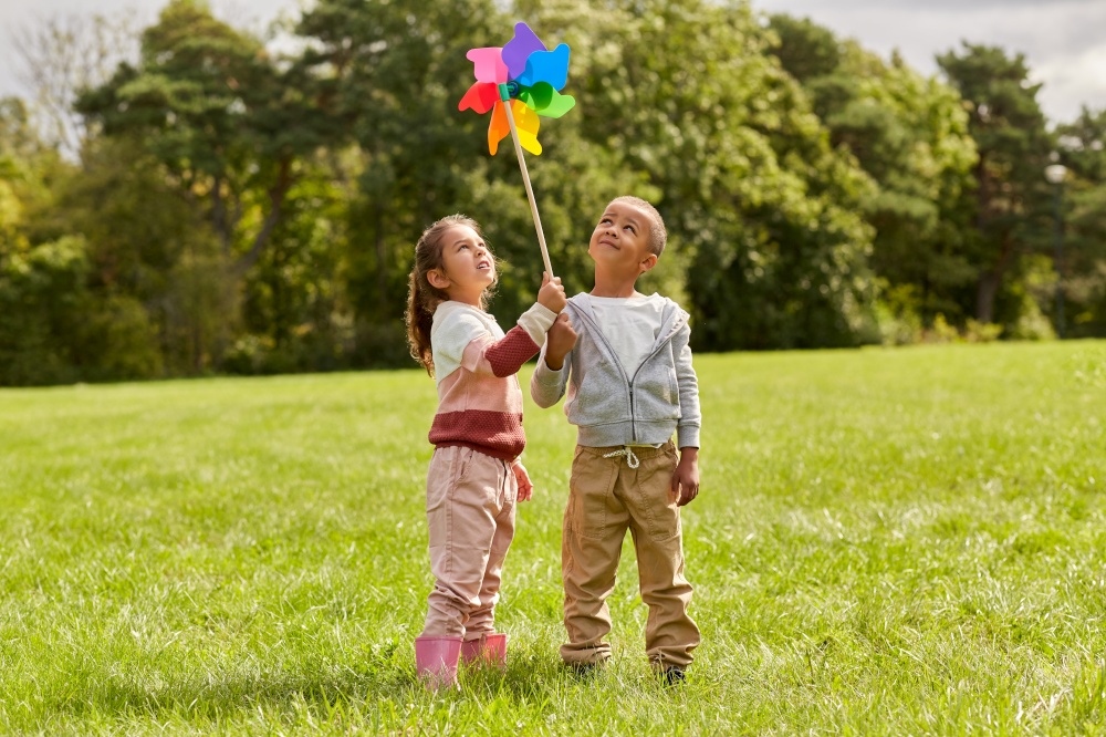 childhood, leisure and people concept - happy kids with pinwheel having fun at park. happy kids with pinwheel having fun at park