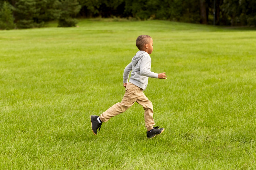 childhood, leisure and people concept - happy little boy running on green field at park. happy little boy running at park