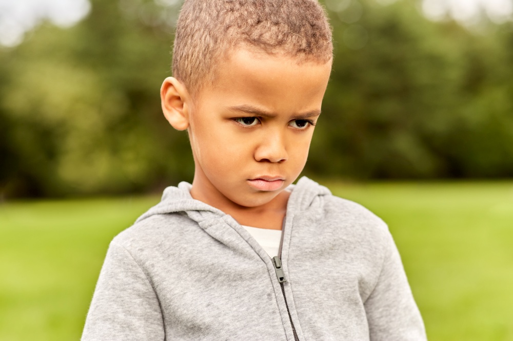 childhood, emotion and people concept - portrait of unhappy little boy at park. portrait of unhappy little boy at park