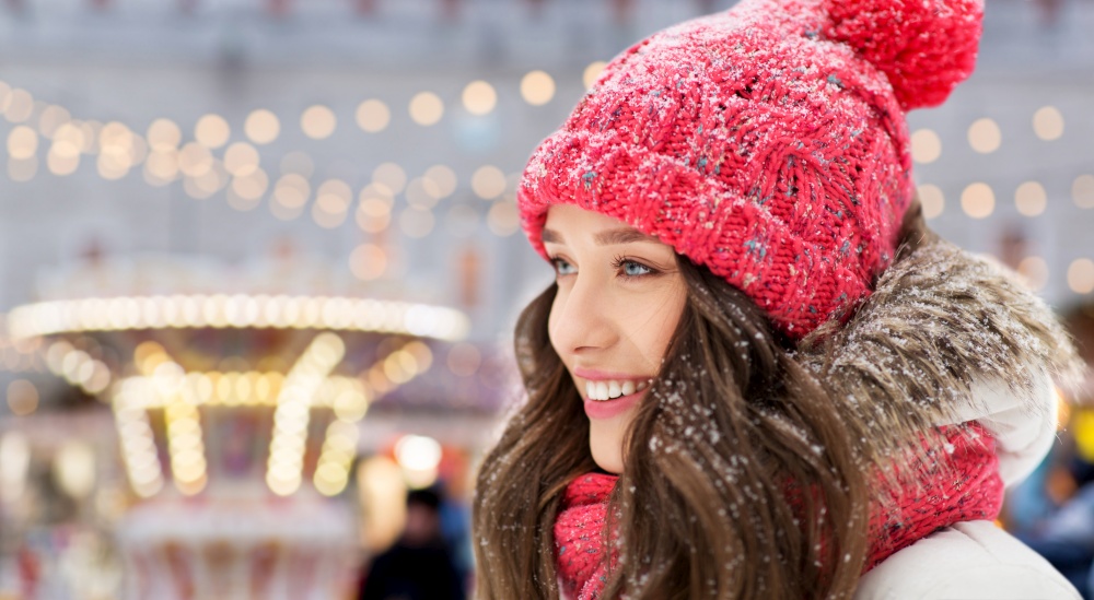 people, season and winter holidays concept - portrait of happy smiling teenage girl or young woman over christmas lights in amusement park on background. happy teenage girl in winter over christmas lights