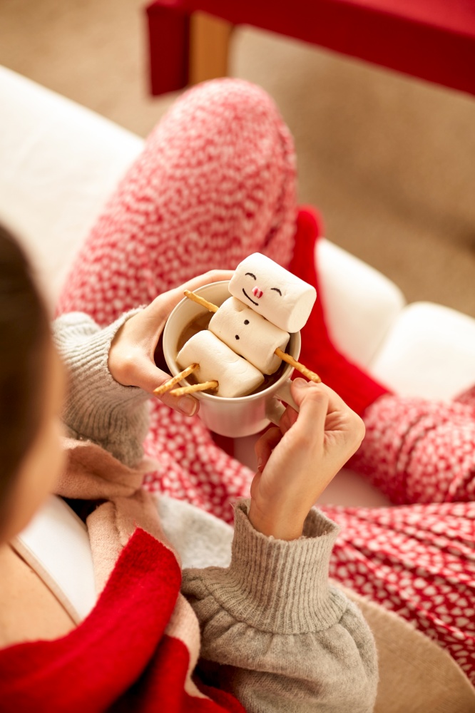christmas, winter holidays and leisure concept - close up of hands holding mug with marshmallow snowman at home. hands with marshmallow snowman in mug on christmas