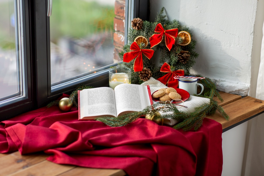 winter holidays and leisure concept - open book, fir branch, oatmeal cookies, coffee and christmas decorations on window sill at home. book, cookies, cup of coffee and christmas decor