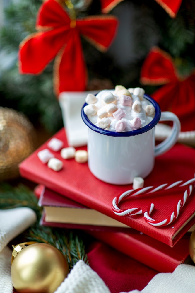 winter holidays, christmas and celebration concept - close up of camp mug with whipped cream and marshmallow, candy canes, books and decorations on window sill at home. cup of whipped cream with marshmallow on christmas