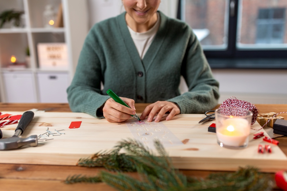 winter holidays and hobby concept - close up of smiling woman with template drawing number one on tag and making advent calendar on christmas. woman with template and marker drawing number