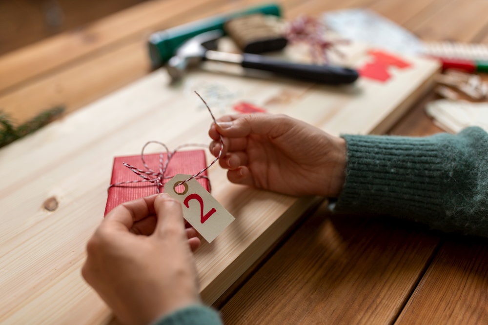winter holidays and hobby concept - close up of woman with box and rope packing christmas gift or making advent calendar at home. woman making advent calendar on christmas at home