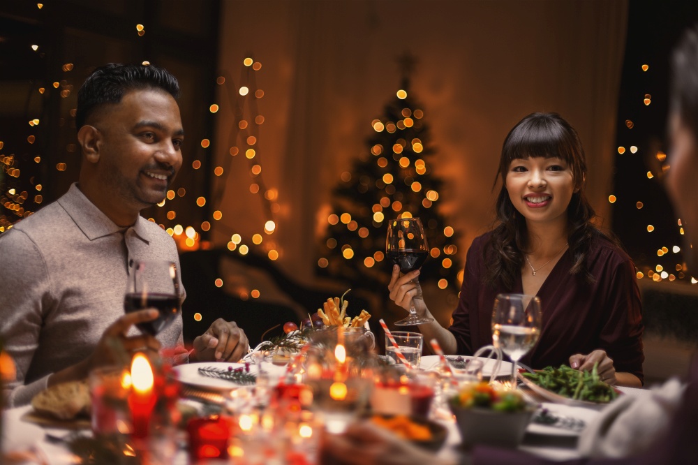 holidays, party and celebration concept - happy friends having christmas dinner at home and drinking wine. happy friends drinking wine at christmas party