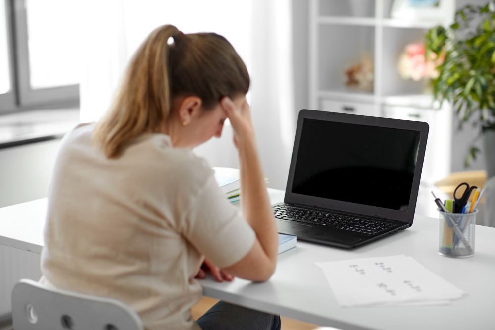 distant education, remote job and health concept - tired female teacher with laptop computer having headache at home office. tired teacher with laptop having headache at home