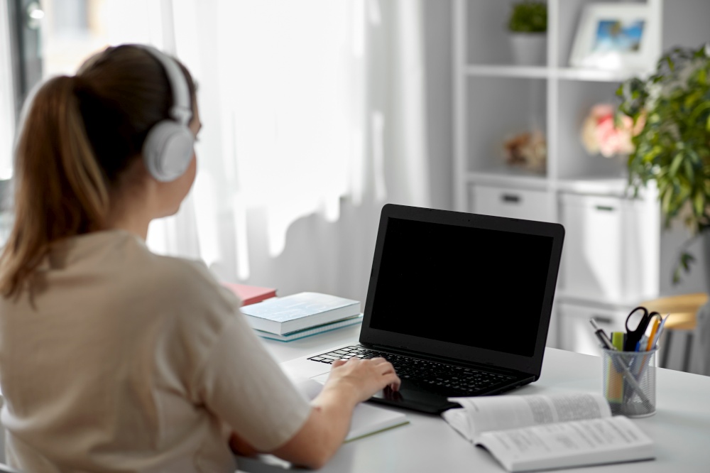 education, online school and distant learning concept - student woman in headphones with laptop computer, notebook and book at home. student woman in headphones with laptop and book