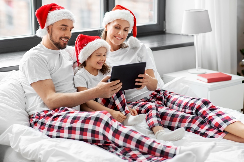 family, winter holidays and people concept - happy mother, father and little daughter with tablet pc computer in bed at home on christmas. happy family with tablet pc in bed on christmas