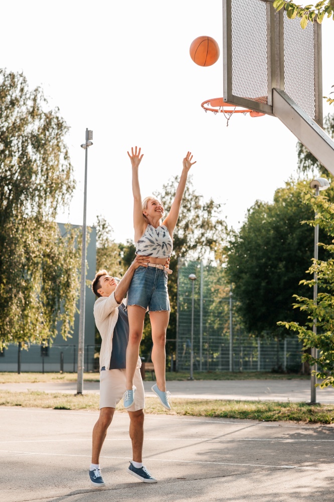 summer holidays, sport and people concept - happy young couple with ball playing on basketball playground. happy couple playing on basketball on playground
