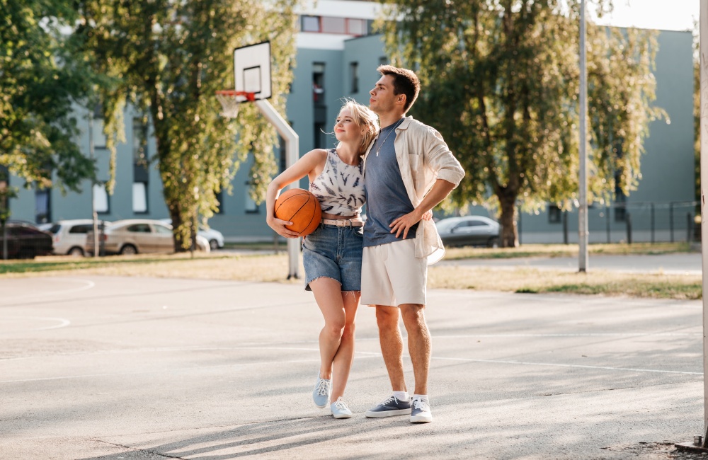 sport, love and people concept - happy young couple with ball hugging on basketball playground. happy couple with ball on basketball playground