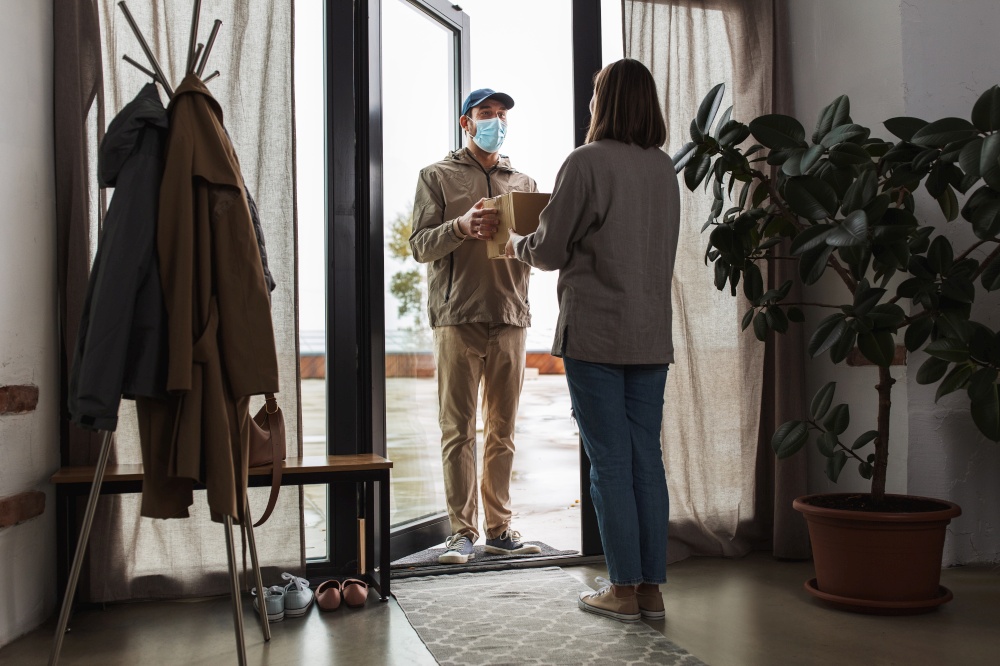 health protection, safety and pandemic concept - delivery man in face protective mask with parcel box and female customer at home. delivery man in mask with box and customer at home