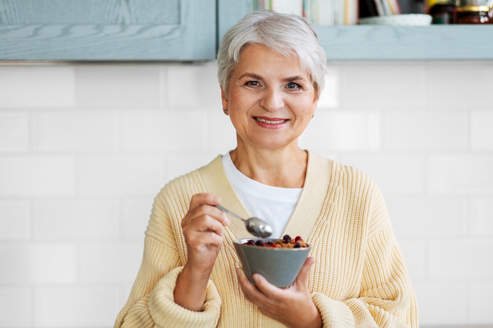 breakfast, food and people concept - happy smiling woman with spoon eating cereal on kitchen at home. woman with cereal for breakfast on kitchen at home