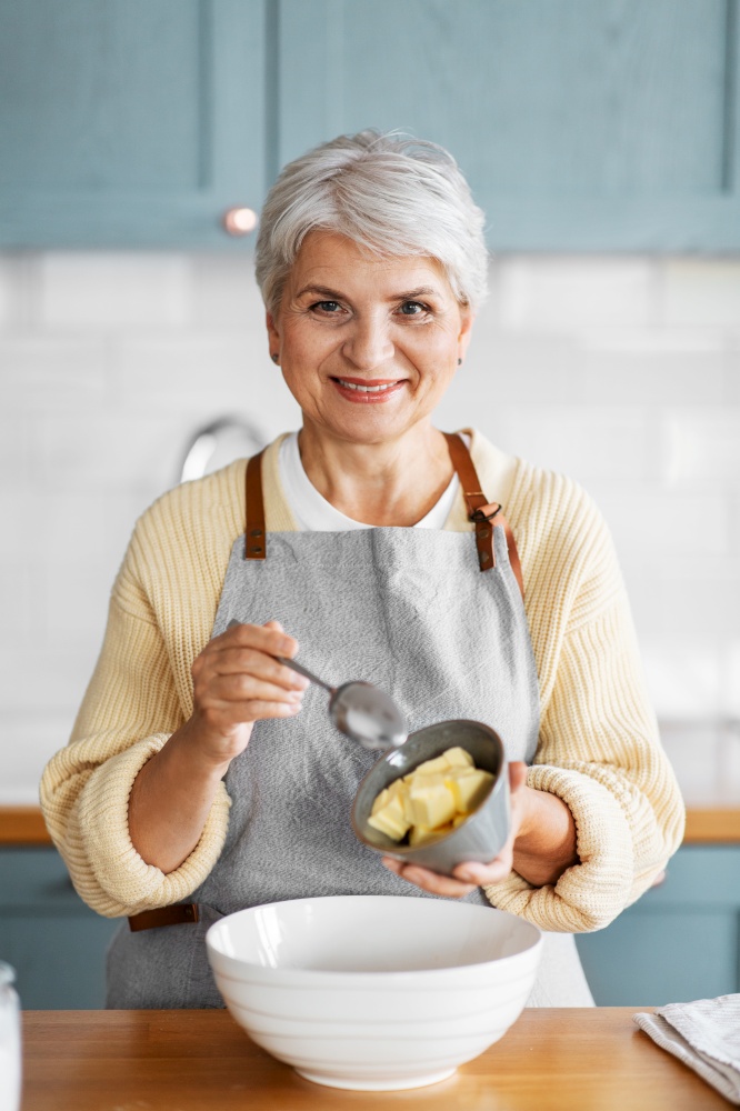 people and culinary concept - happy smiling woman cooking food on kitchen at home and adding butter. happy woman cooking food on kitchen at home