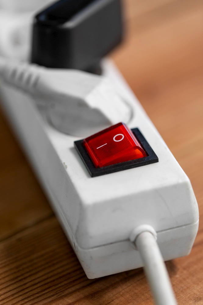 electricity, energy and power consumption concept - close up of socket with plugs, charger and red switch button on wooden floor. close up of socket with plugs and charger on floor