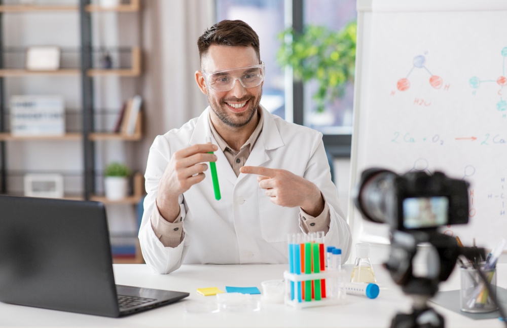 distant education, school and video blogging concept - happy smiling male chemistry teacher with camera and test tube having online class at home office. chemistry teacher with camera having online class