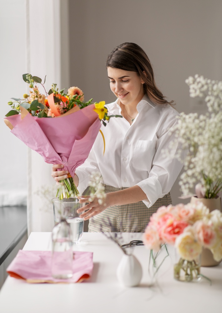 people, gardening and floral design concept - happy woman or floral artist putting bunch of flowers in vase at home. happy woman arranging flowers in vase at home