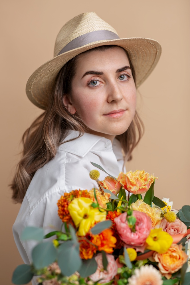 people, portrait and floral design concept - pensive woman in straw hat holding bunch of flowers over beige background. woman in straw hat holding bunch of flowers