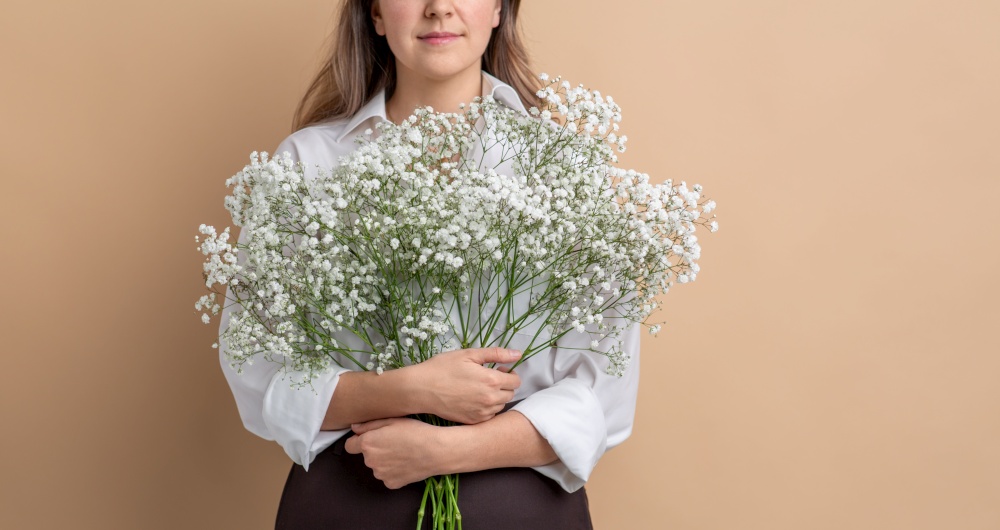 people and floral design concept - close up of woman holding bunch of gypsophila flowers over beige background. close up of woman holding bunch of flowers