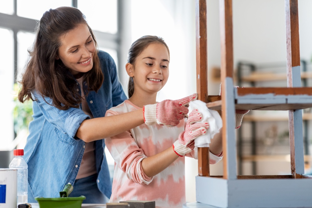 renovation, diy and home improvement concept - happy smiling mother and daughter cleaning old round wooden table surface with tissue. mother and daughter cleaning old table with tissue