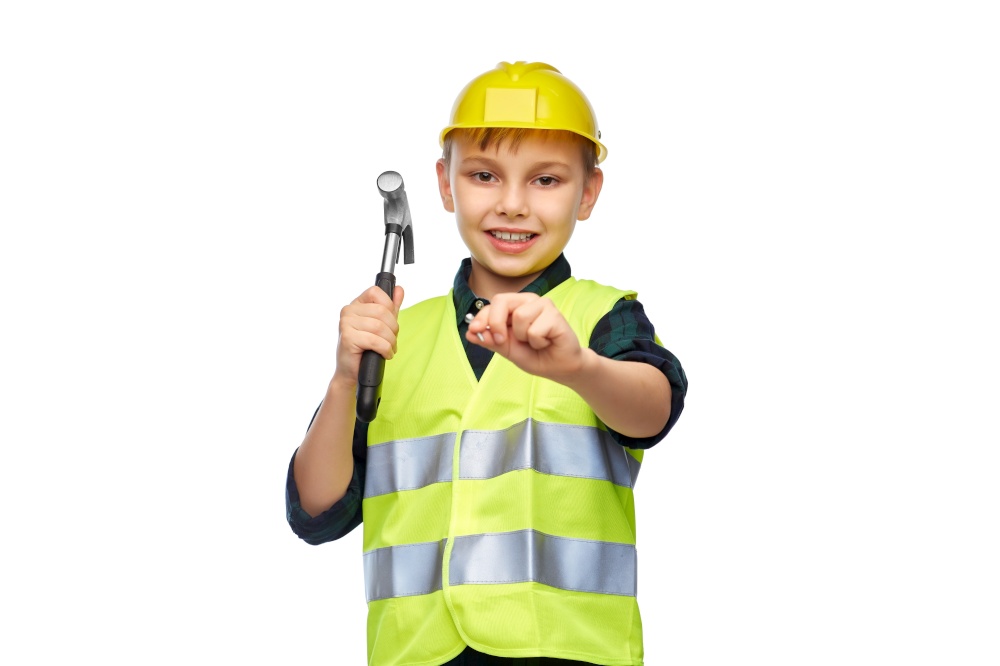building, construction and profession concept - happy smiling little boy in protective helmet and safety vest with hammer nailing nail over white background. boy in protective helmet with hammer nailing nail