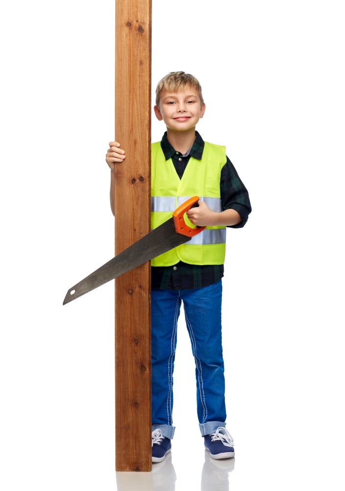 building, carpentry and profession concept - happy smiling little boy in protective helmet and safety vest with saw and wooden board over white background. little boy in safety vest with saw and board
