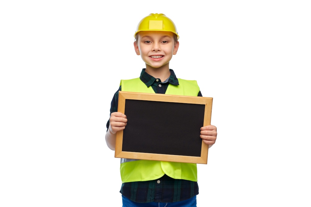 building, construction and profession concept - happy smiling little boy in protective helmet and safety vest holding chalkboard over white background. little boy in protective helmet holding chalkboard