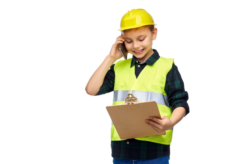 building, construction and profession concept - happy smiling little boy in protective helmet and safety vest with clipboard calling on smartphone over white background. boy in helmet with clipboard calling on phone