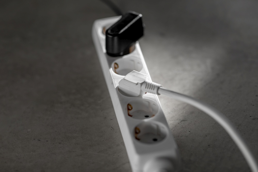 electricity, energy and power consumption concept - close up of socket with plugs and charger on concrete floor. close up of socket with plugs and charger on floor