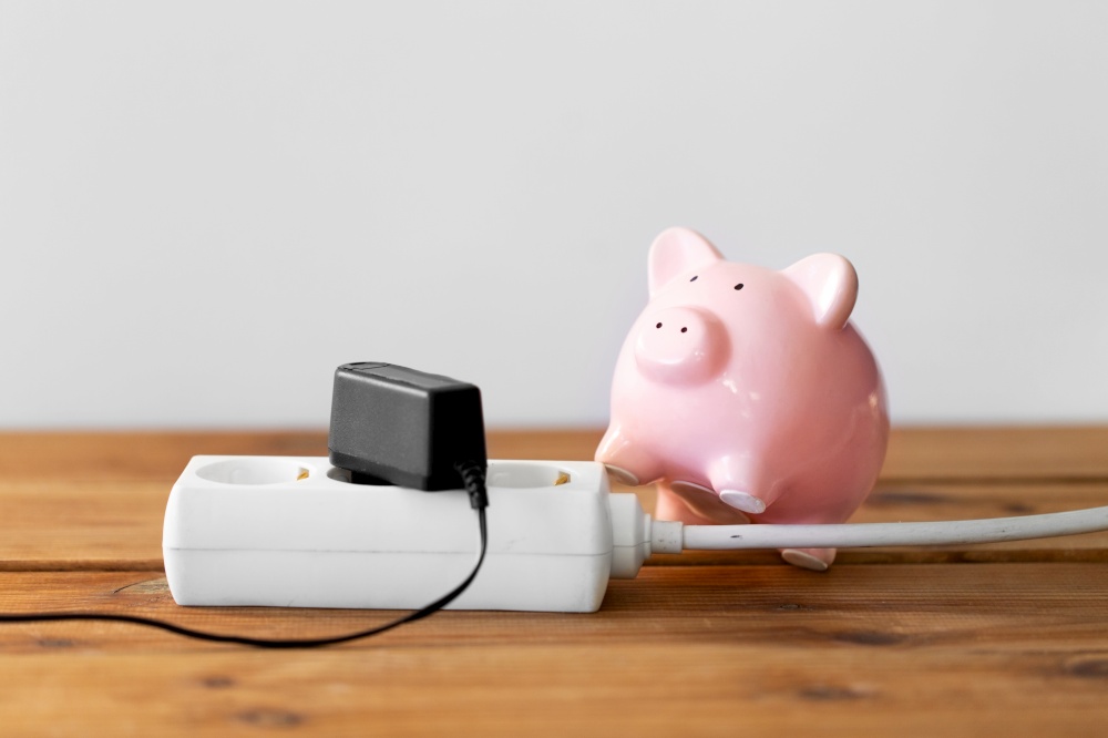 electricity, energy crisis and power consumption concept - close up of piggy bank and electric socket. close up of piggy bank and electric socket