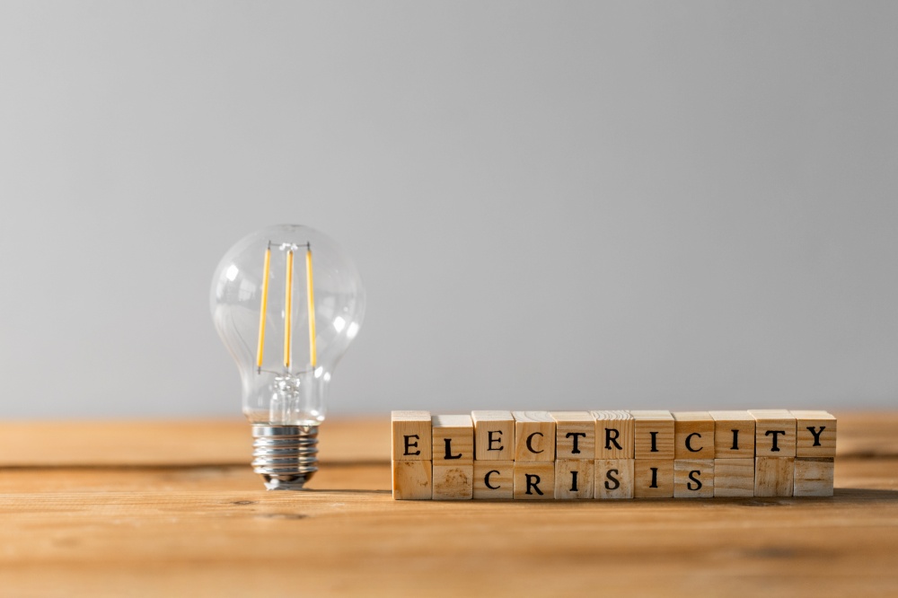 energy and power consumption concept - close up of lightbulb and blocks with electricity crisis words on wooden table. lightbulb and blocks with electricity crisis words