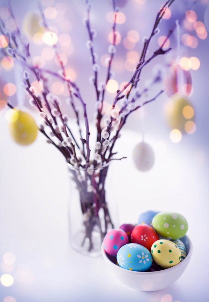 holidays and object concept - close up of pussy willow branches and colored easter eggs in vase on table in violet shades over festive lights. close up of easter eggsand pussy willow branches