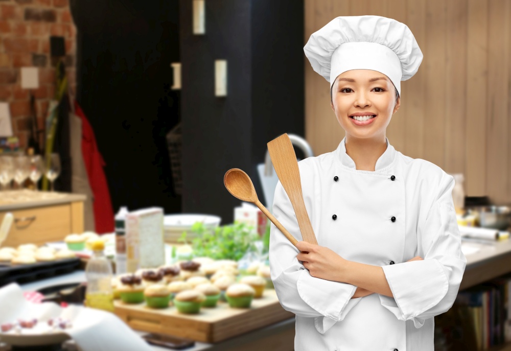 cooking, culinary and people concept - happy smiling female chef in toque with wooden spoon over restaurant kitchen background. happy smiling female chef with wooden spoon