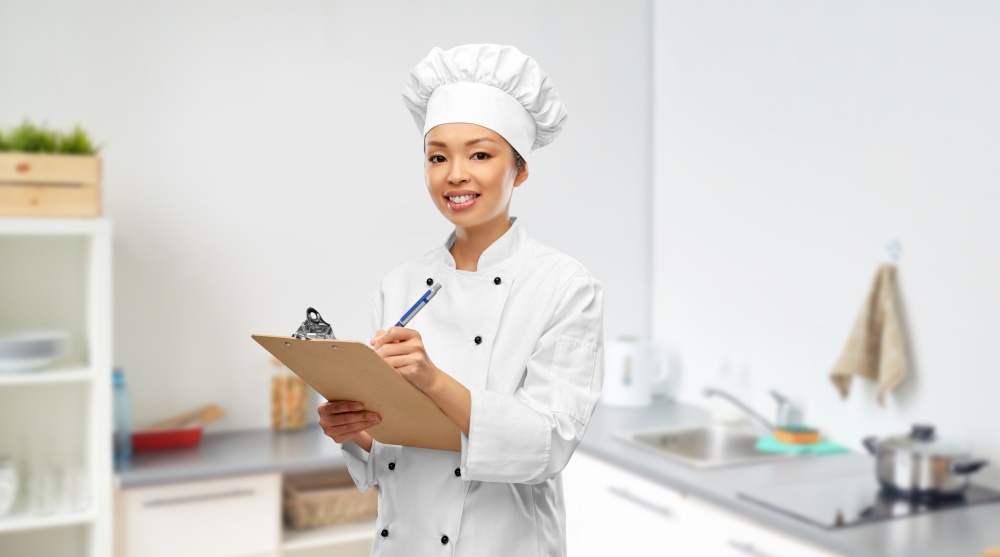 cooking, culinary and people concept - happy smiling female chef with clipboard and pen over kitchen background. smiling female chef with clipboard and pen