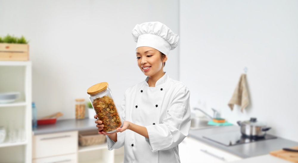 cooking, culinary and people concept - happy smiling female chef holding jar with pasta over kitchen background. smiling female chef holding jar with pasta