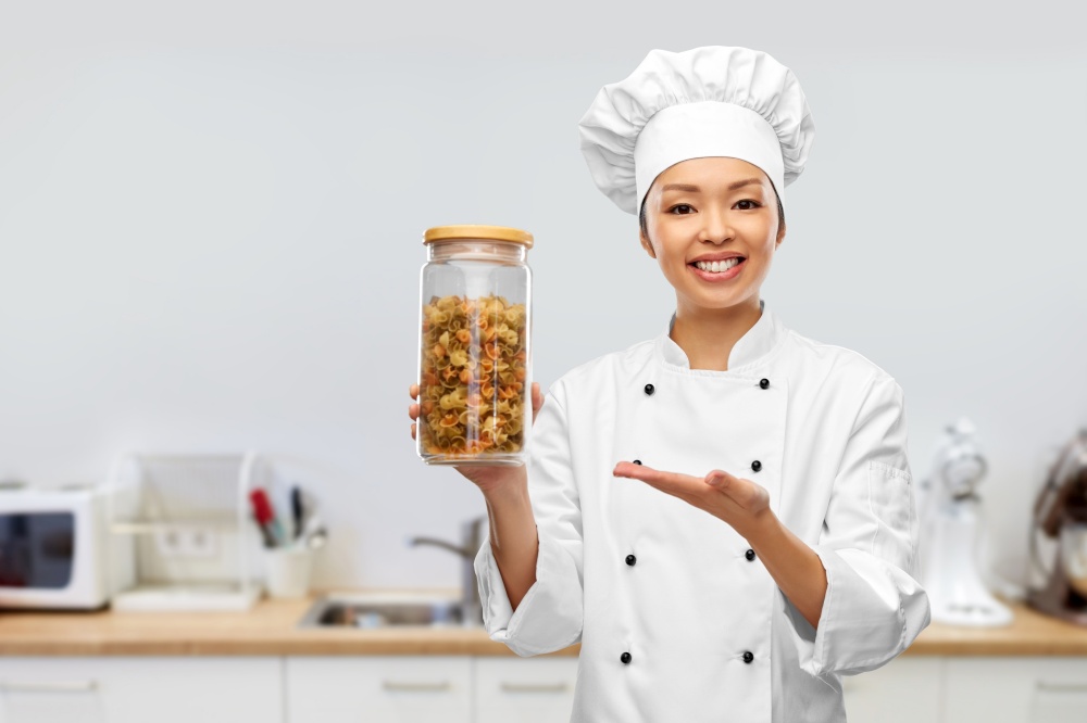 cooking, culinary and people concept - happy smiling female chef holding jar with pasta over kitchen background. smiling female chef holding jar with pasta