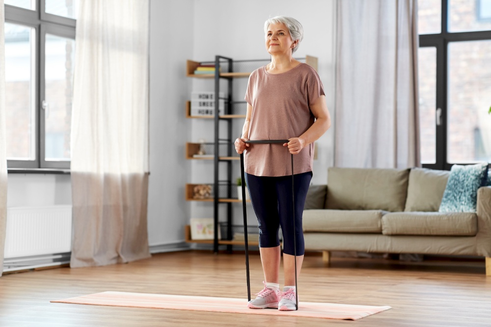 sport, fitness and healthy lifestyle concept - smiling senior woman exercising with resistance band on mat at home. senior woman exercising with elastic band at home