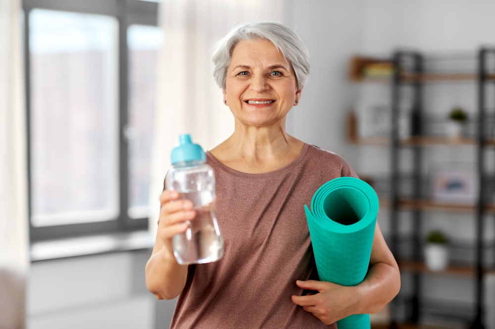 sport, fitness and healthy lifestyle concept - smiling senior woman with yoga mat and bottle of water at home. senior woman with yoga mat and bottle of water