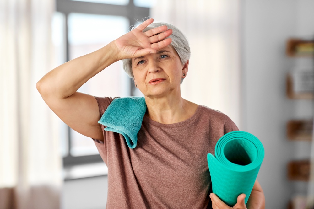 sport, fitness and healthy lifestyle concept - tired senior woman with yoga mat and towel at home. tired senior woman with yoga mat and towel