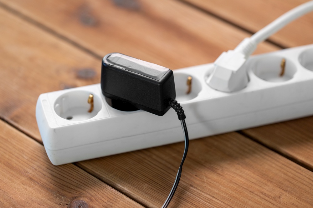 electricity, energy and power consumption concept - close up of socket with plugs and charger on wooden floor. close up of socket with plugs and charger on floor