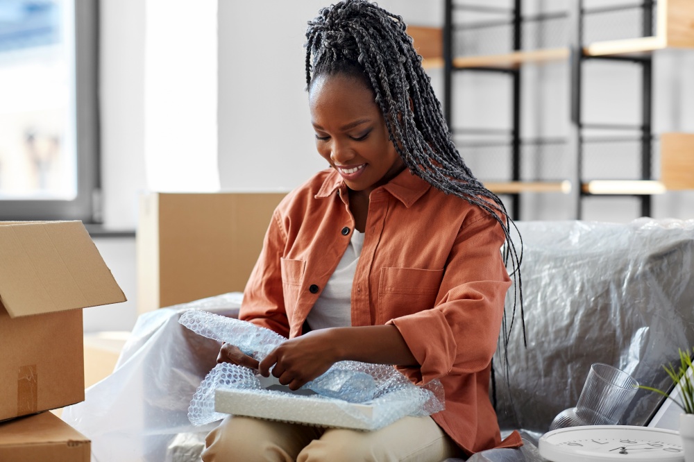 moving, people and real estate concept - happy smiling woman packing boxes sitting on sofa at home. happy woman packing boxes and moving to new home