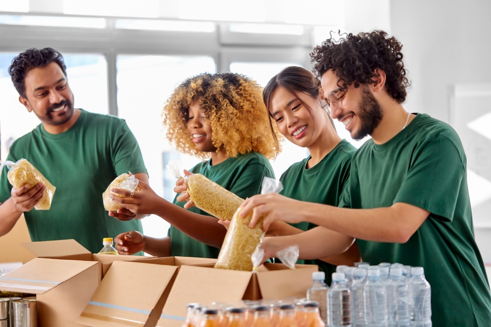 charity, donation and volunteering concept - international group of happy smiling volunteers packing food in boxes at distribution or refugee assistance center. happy volunteers packing food in donation boxes