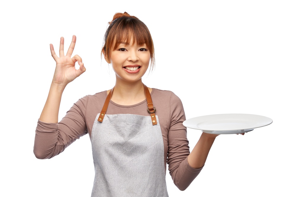 cooking, culinary and people concept - happy smiling female chef or waitress in apron with empty plate over white background. happy woman in apron with empty plate