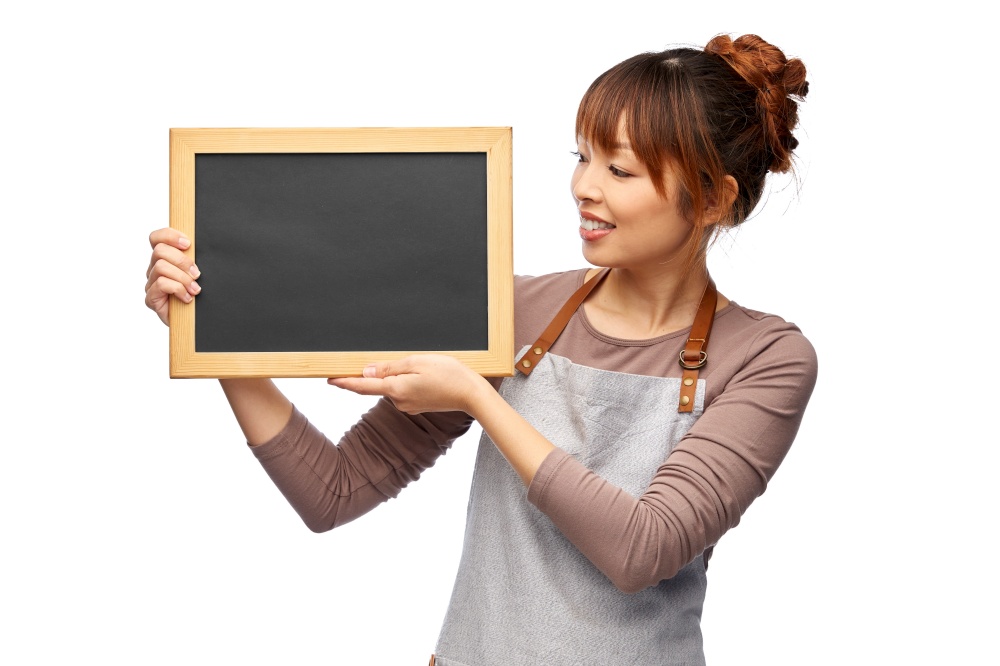 cooking, culinary and people concept - happy smiling female chef or waitress in apron with chalkboard over white background. happy woman in apron with chalkboard