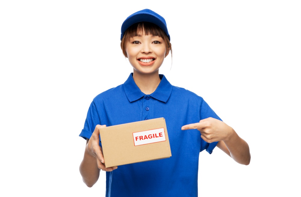 profession, job and people concept - happy smiling delivery woman in blue uniform holding parcel box with fragile mark over white background. happy smiling delivery woman holding parcel box