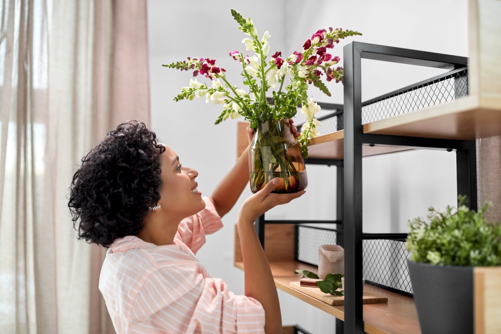 home improvement, decoration and people concept - happy smiling woman placing flowers to shelf. woman putting flowers on shelving at home