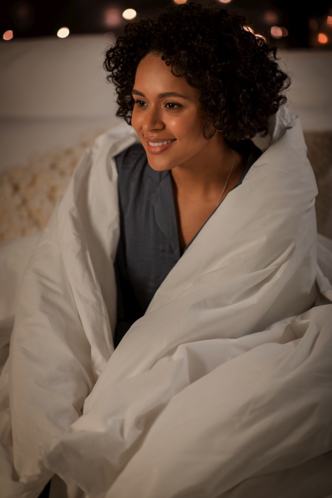 people, bedtime and rest concept - happy smiling woman wrapped in blanket sitting in bed at night. woman wrapped in blanket sitting in bed at night
