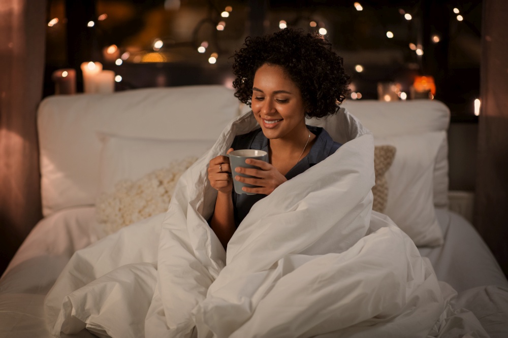 people, bedtime and rest concept - happy smiling woman in pajamas with coffee sitting in bed at night. happy woman with coffee sitting in bed at night